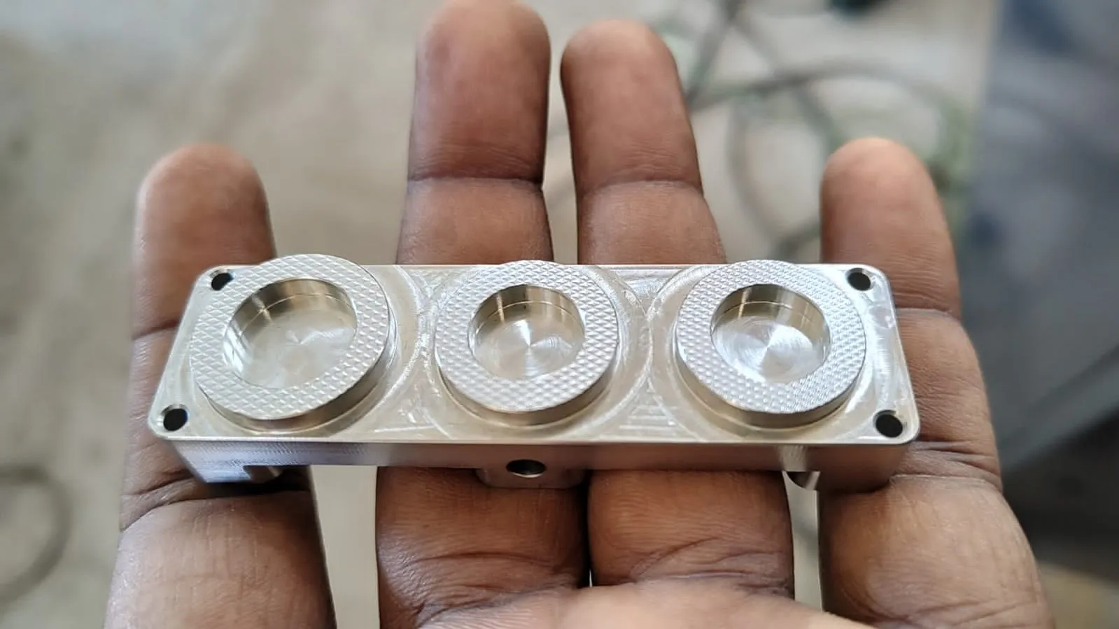 A machined aluminum part with three knurled rings, held in a hand