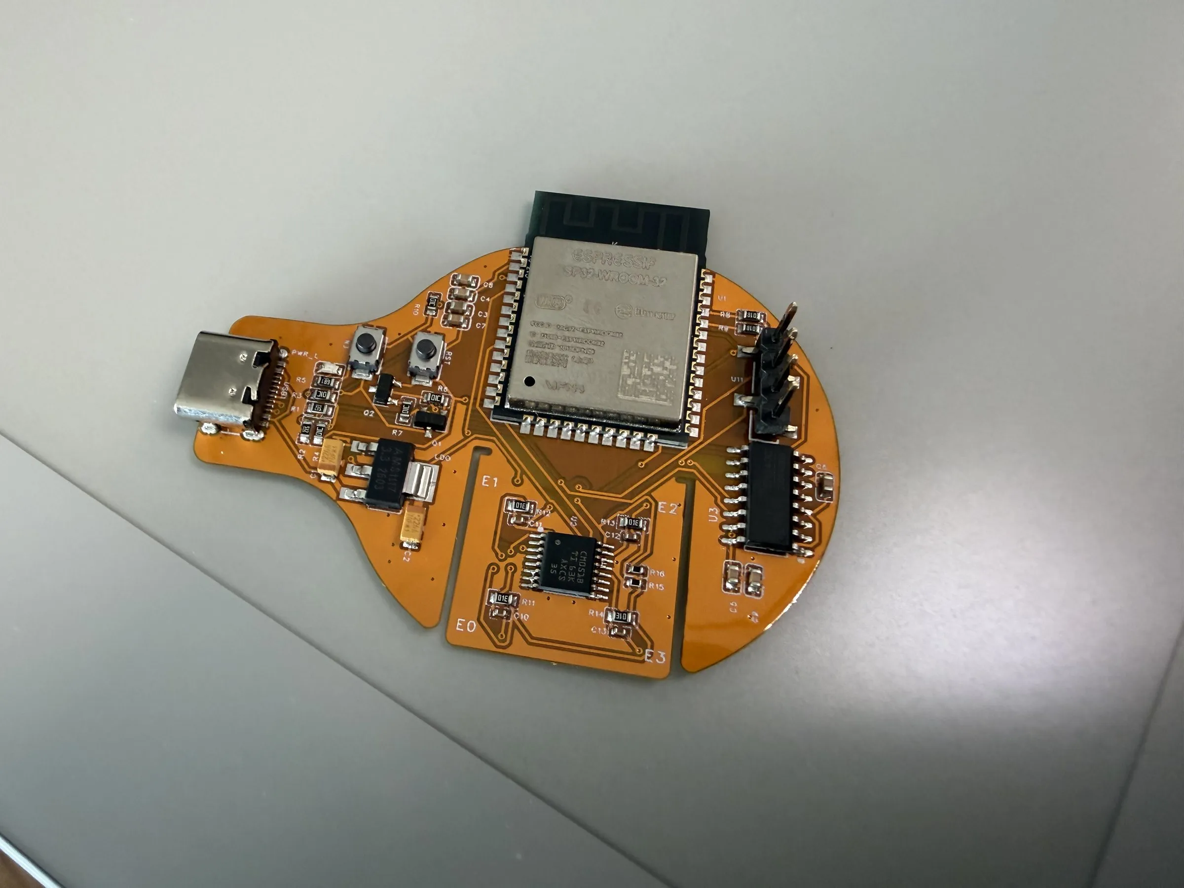 Orange flex PCB prototype of the EMG wearable, component side, with an ESP32 module and USB-C connector
