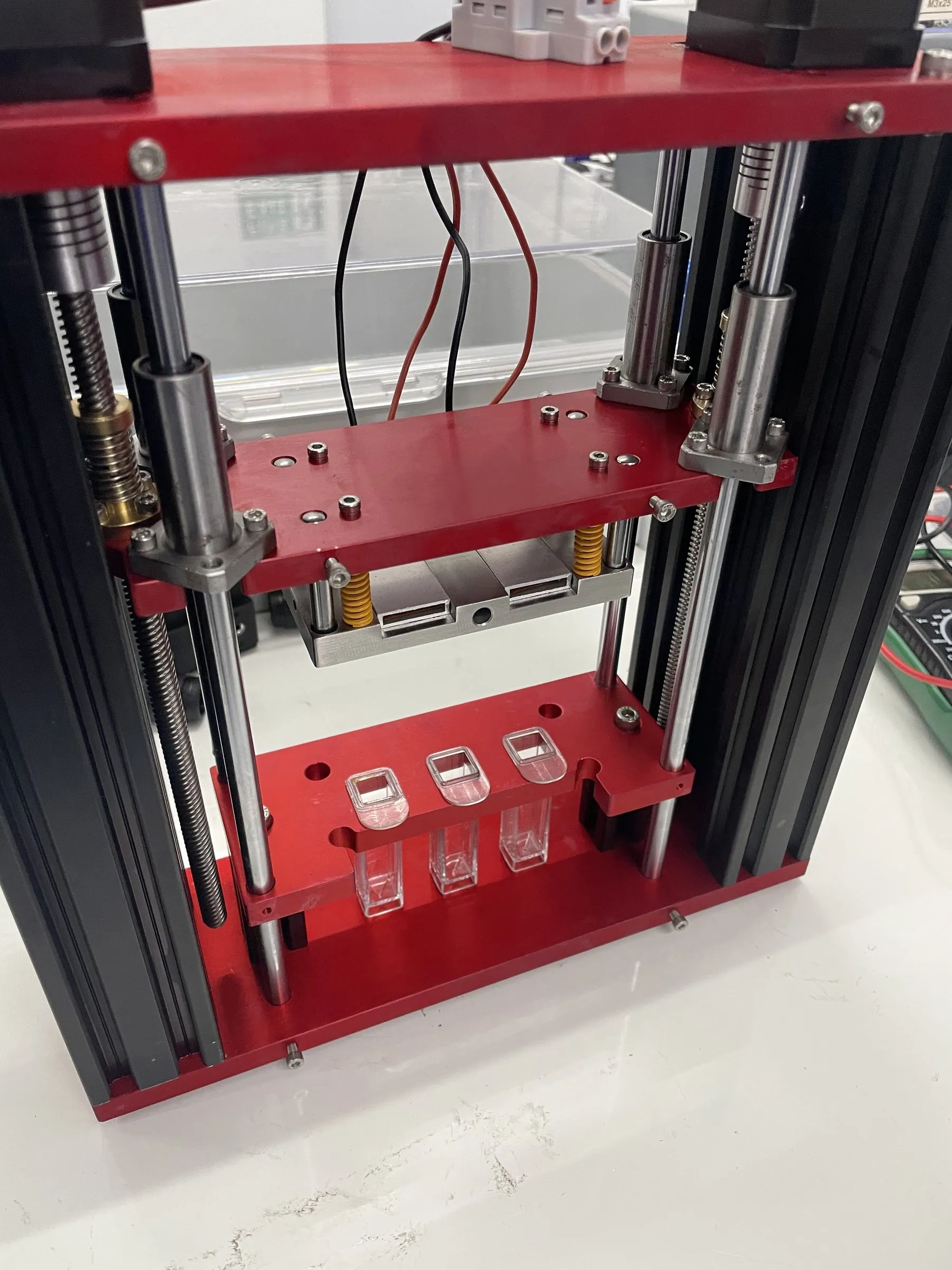 Red machined plates on lead screws and guide rods holding three clear cuvettes