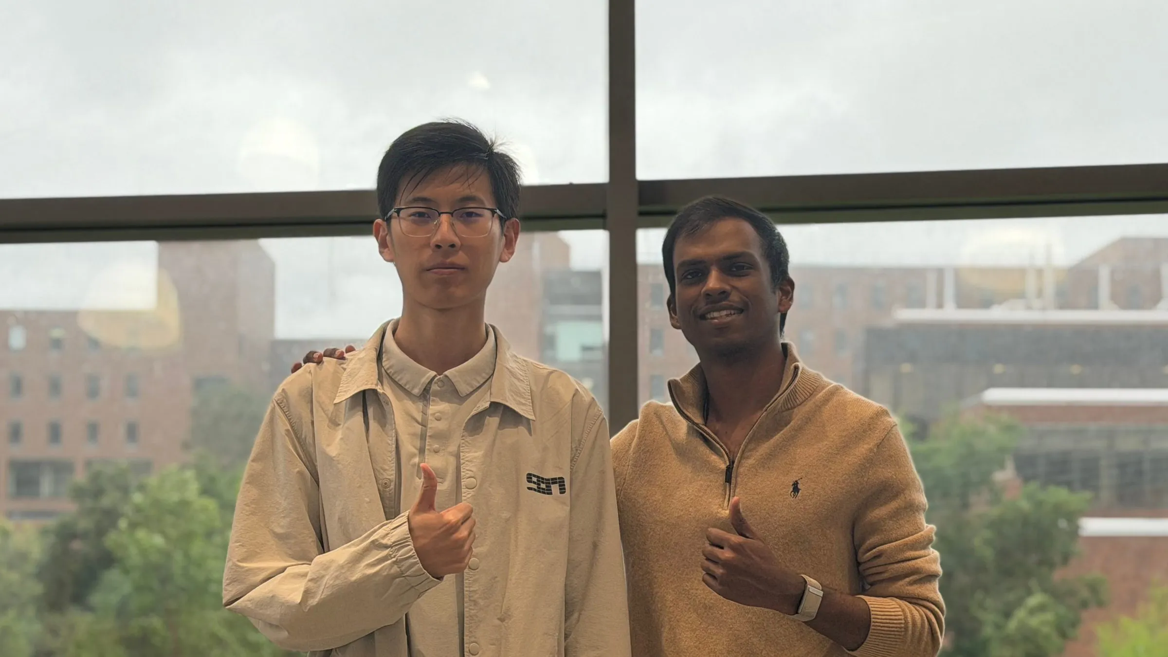Kumar and a Pebble Robotics teammate giving a thumbs-up in front of a large window