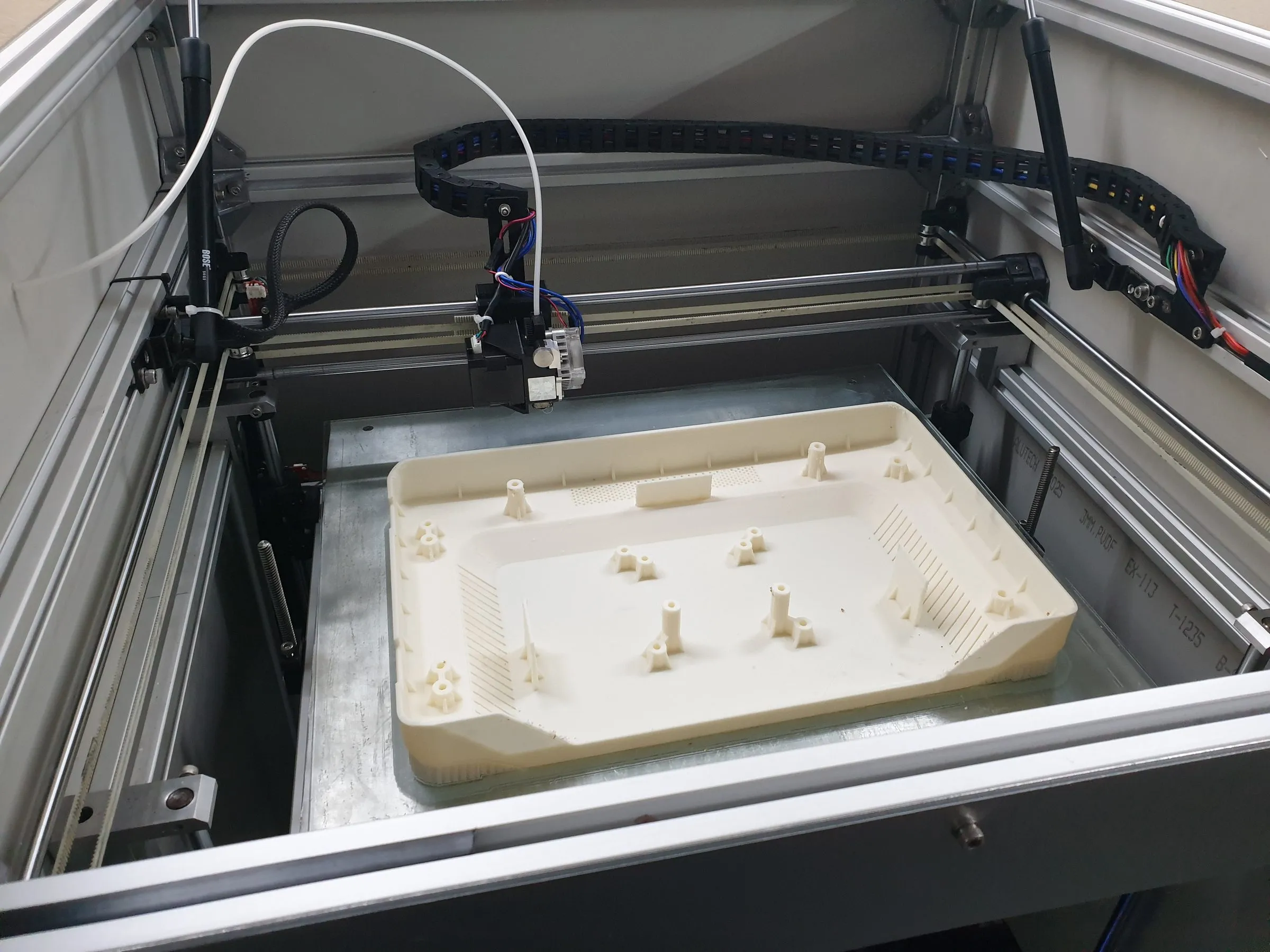 A large tray printing inside a large-format printer, with a cable chain on the gantry