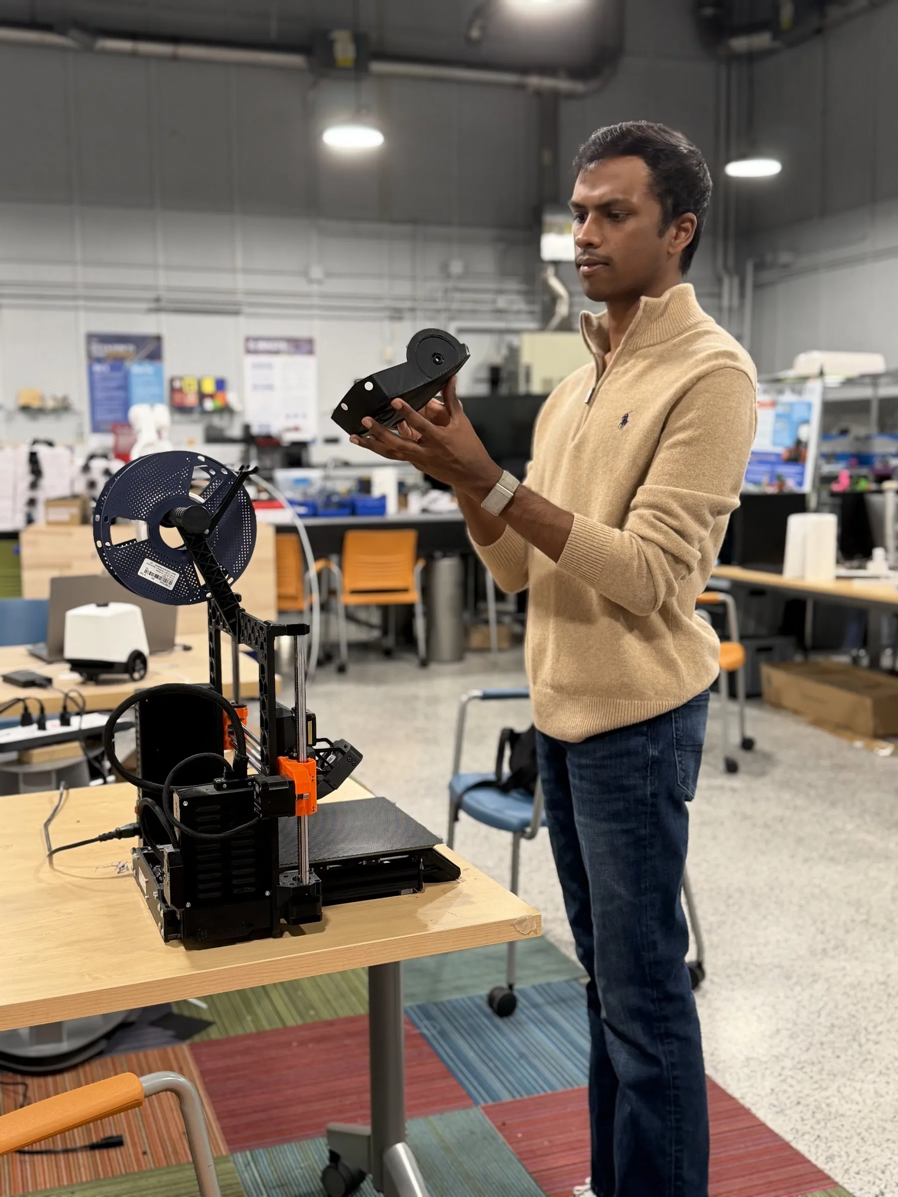 Kumarappan Muthuraman holding a 3D-printed part in a makerspace, next to a 3D printer