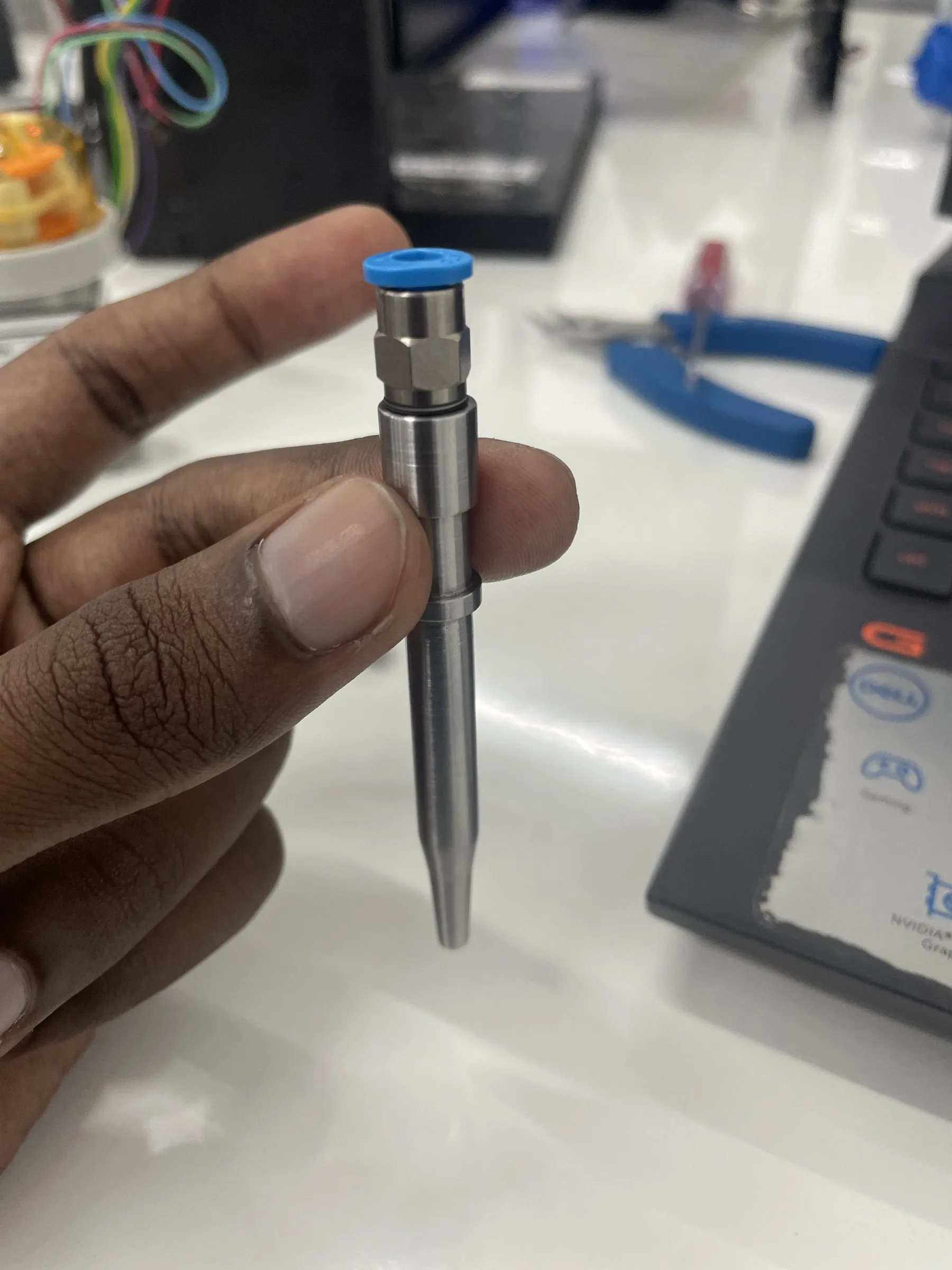 Hand holding a machined stainless-steel pipette probe with a blue fitting